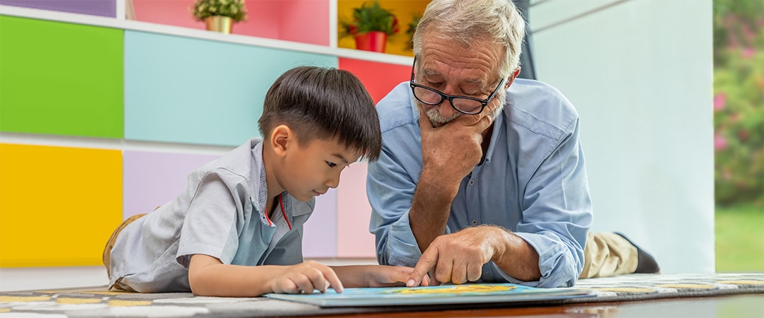 An elderly man reading with a preschool age boy.